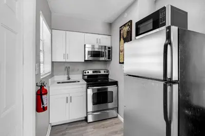 a kitchen with white cabinets and a stainless steel refrigerator at Chic 1BR Getaway Near FLL Airport + 6 MN to Ocean in Dania Beach