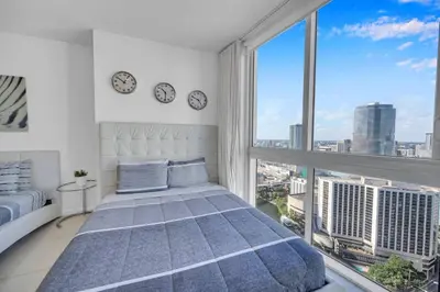 a bedroom with a bed and a large window with clocks at Sun, Style and Skyline Modern Icon Brickell 2BR in Miami