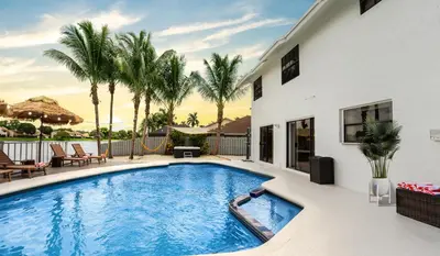 a swimming pool in front of a house with palm trees at Waterfront Villa with Beach, Game Room, Cinema and Spa in Pembroke Pines