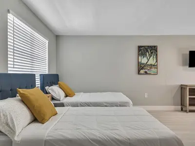a bedroom with two beds and a tv on the wall at Beachside 1BR in Hollywood | Parking + WiFi in Dania Beach