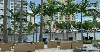 a patio with chairs and palm trees next to a body of water at Modern Condo by the Beach, Water Taxi Stop, Prime Location! in Fort Lauderdale