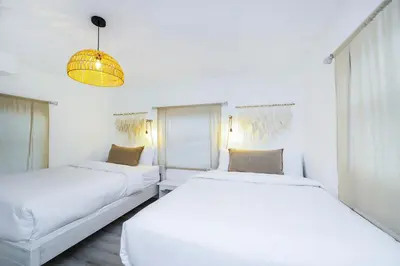 two beds in a white room with a chandelier at Alton Rd By At Mine Hospitality in Miami Beach