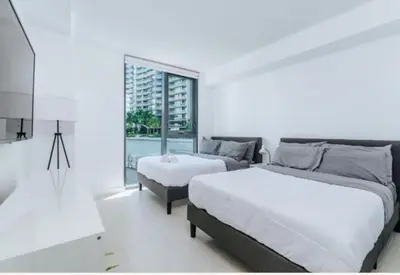 a white bedroom with two beds and a window at Cozy 2BR Apt at Brickell free parking in Miami