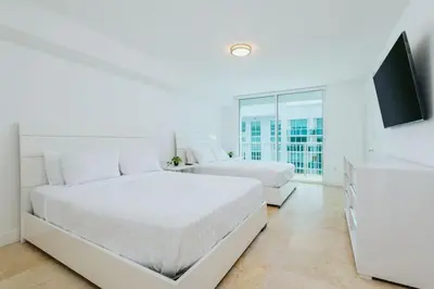 a white bedroom with two beds and a flat screen tv at Bright and Cozy 2 Bedroom in Miami