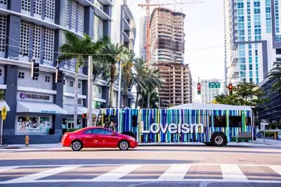 a red car driving past a bus on a city street at Lovely 2BR in the Heart of Brickell Free Parking in Miami