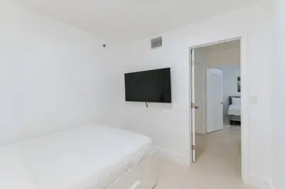 a white bedroom with a bed and a flat screen tv at Amazing 2BR at Brickell Free Parking in Miami