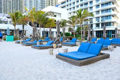 a sandy beach with blue lounge chairs and palm trees at Beachfront Luxury Condo in Hollywood in Hollywood