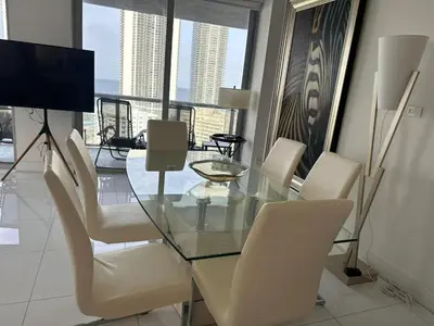 a dining room with a glass table and white chairs at Family Oriented Apartments with unbelievable views in Hallandale Beach
