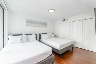 two beds in a bedroom with white walls and wood floors at 3 bedroom stunning apt brickell in Miami