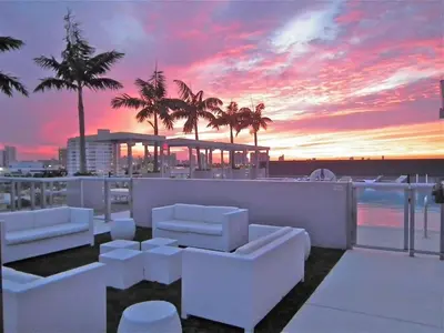 a sunset over a building with white furniture and palm trees at Large Beach Suite Rooftop Pool by Convention Center in Miami Beach
