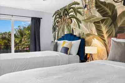 two beds in a bedroom with a mural of palm trees at Walk To Coral Gables | SLEEP 8| Free BEACH Package in Miami