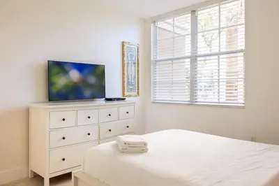 a white bedroom with a white dresser and a tv at Luxe 3BR Apartment with Great Patio at Yacht Club in Aventura