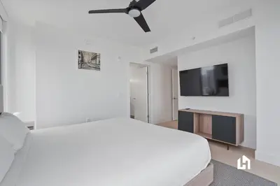 a white bedroom with a bed and a flat screen tv at Stylish Sky-High Condo with Pool and Gym in Miami
