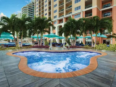 a swimming pool at a resort with palm trees and umbrellas at Marriott's BeachPlace Towers 2BR Apartment with Resort Access in Fort Lauderdale