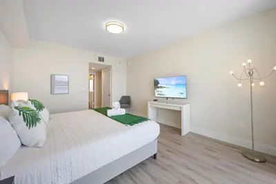 a white bedroom with a bed and a desk at Golden Bay 504 in Sunny Isles Beach