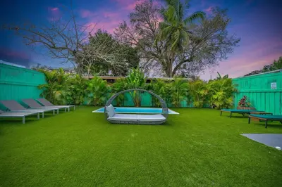 a green yard with benches and a bed on the grass at La Casa Flora Private PoolHot tubSleeps 18 in Miami