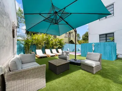 a patio with chairs and a blue umbrella at Villa mi Amor Walkable Pool & Games in Miami