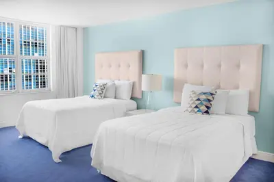 a bedroom with two white beds and a blue floor at Seacoast Suites on Miami Beach in Miami Beach