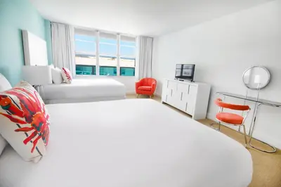 a white bedroom with two beds and a chair at Seacoast Suites on Miami Beach in Miami Beach