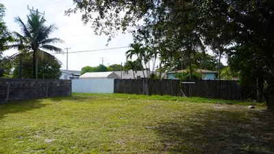 a backyard with a fence and a yard with a tree at Charming Historic Home with Modern Comforts in Opa-locka