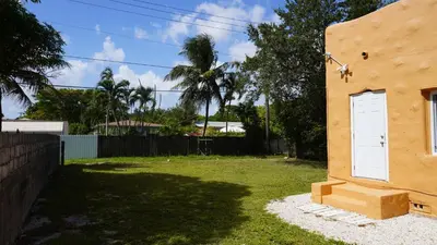 a house with a white door next to a yard at Charming Historic Home with Modern Comforts in Opa-locka
