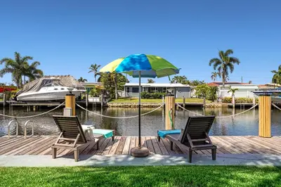 two chairs and an umbrella on a dock with a boat at Waterfront Retreat Home Dania Beach in Dania Beach
