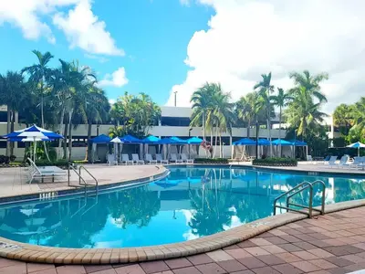 a pool at a resort with palm trees and blue umbrellas at Luxury Beach & City View Condo 5 min walk to beach in Sunny Isles Beach