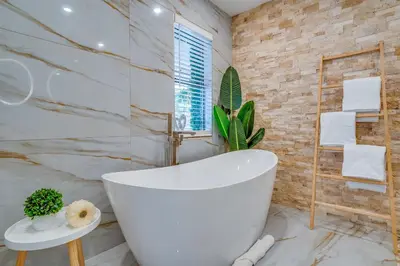 a bathroom with a white tub and a stone wall at Fox Garden Luxury Boho Near Downtown & Beach in Fort Lauderdale