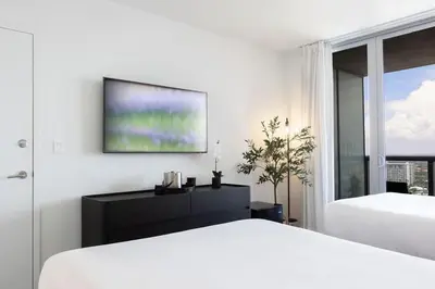 a white bedroom with two beds and a flat screen tv at Epic 29th-Floor Studio at Beachwalk Resort in Hallandale Beach