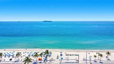 a beach with umbrellas and palm trees and the ocean at Tiffany Topaz - Rooftop Pool, Gym, Walk to Beach in Fort Lauderdale