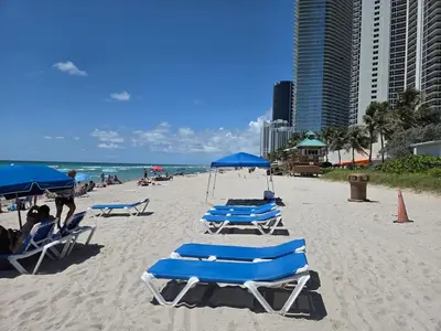 a beach with blue chairs and umbrellas and the ocean at Lujoso Departamento Con VIstas Al Mar- Miami Beach in Sunny Isles Beach