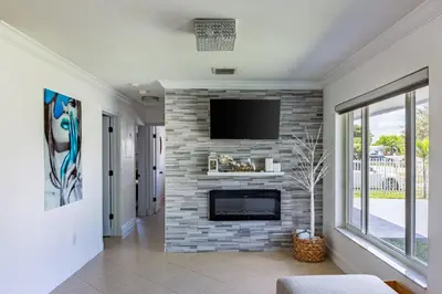 a living room with a stone fireplace with a flat screen tv at Waterfront 3BR with Pool Tiki Hut & Mini Golf in Miami Gardens