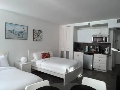 a white room with two beds and a kitchen at Oceanview Studio at Castle Beach Club – Pool, Beach Access, Valet Parking, Gym & More! in Miami Beach