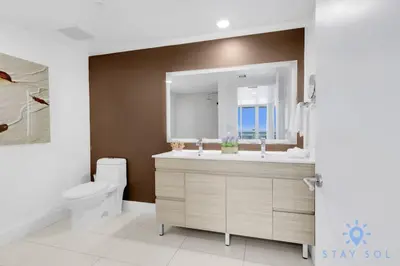 a bathroom with a sink and a toilet and a mirror at Stylish 2BR High-Rise Retreat w Ocean Views in Hallandale Beach
