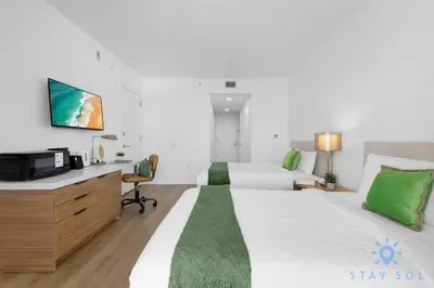 a bedroom with a bed and a desk with a tv at Coastal Retreat Modern Studio w Harbour Views in Hallandale Beach