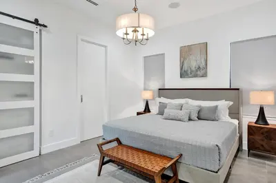 a bedroom with a bed and a bench and a chandelier at New Luxe Contemporary Home 4BR-4BA with Heated Pool, Mini Golf, Pool table in Fort Lauderdale