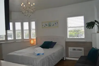 a bedroom with a bed with a chandelier and windows at WATERFRONT STUDIO COZY WITH WATERVIEWs in Miami Beach