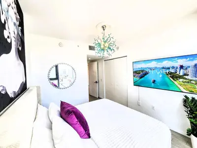 a bedroom with a white bed and a tv on the wall at 3BR Skyline Luxury with a 100 inch TV, Balcony & Prime Miami Location in Miami