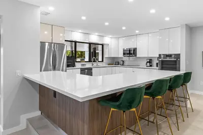 a kitchen with a large white counter and green bar stools at Lakefront Villa Tropical Backy in North Miami Beach