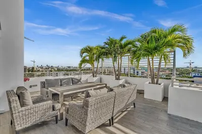 a patio with chairs and a table and palm trees at Waterfront Luxury Kosher Condo with Rooftop Pool, Bay Harbor Islands in Miami Beach