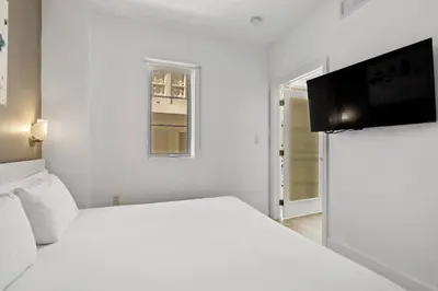 a white bedroom with a bed and a flat screen tv at Miami Ocean Drive 1BR APT & Rooftop Pool Access in Miami Beach