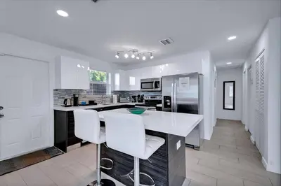a white kitchen with a counter and white chairs at Modern 2BR Near Wynwood and Design District in Miami