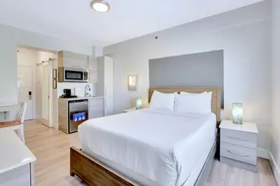 a bedroom with a large white bed and a kitchen at Sunny Beach Studio Steps to Ocean and Nightlife in Miami Beach