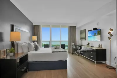 a hotel room with a large bed and a desk and a window at Modern Comfort Steps from the Ocean Breeze in Miami