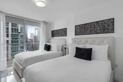 two beds in a white bedroom with a window at Stunning 2B2B Ocean and City Views with Free Parking in Miami