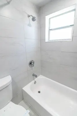 a white bathroom with a tub and a toilet at Spacious North Miami Studio | 2 Queen Beds in North Miami