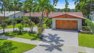 a house with a garage and palm trees at Vista Azul Lake Front Home with Hot Tub and Swim Spa, Fishing Dock, Gym, Game Room with Darts, Ping Pong, A Pool Table and more! in Miami Lakes