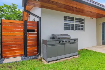 a barbecue grill in a yard next to a house at Vista Azul Lake Front Home with Hot Tub and Swim Spa, Fishing Dock, Gym, Game Room with Darts, Ping Pong, A Pool Table and more! in Miami Lakes