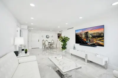 a white living room with a white couch and a tv at Oceanfront Escape with Resort Amenities Gym Pools and Sauna 1408 in Miami Beach