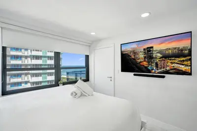 a white bedroom with a large tv on the wall at Oceanfront Escape with Resort Amenities Gym Pools and Sauna 1408 in Miami Beach